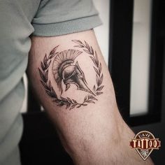 a man's arm with a spartan helmet and laurel wreath tattoo on the forearm