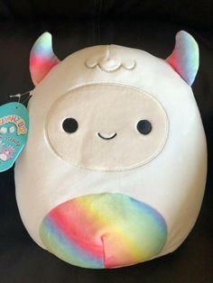 a white stuffed animal with a rainbow colored mane on it's face and eyes