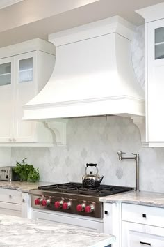 a kitchen with white cabinets and marble counter tops, an oven hood over the stove