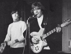 two young men are playing guitars and singing into microphones while another man stands behind them