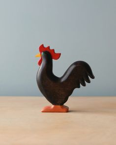 a small wooden rooster figurine sitting on top of a table next to a gray wall