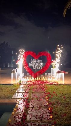 a heart - shaped sign is lit up in the night with candles and flowers on it