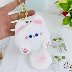 a hand holding a keychain with a white stuffed animal on it