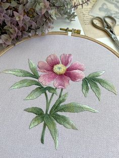 a pink flower with green leaves is embroidered onto a white fabric in front of purple flowers