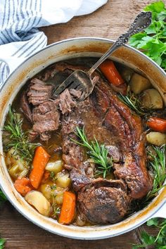 pot roast with carrots, potatoes and parsley in it on a wooden table