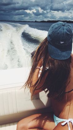 a woman sitting on the back of a boat looking out at the water while wearing a hat