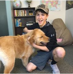 a young boy kneeling down next to a brown dog