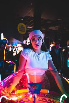 a woman in white shirt sitting on top of a spinning machine with neon lights around her