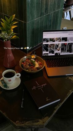 a laptop computer sitting on top of a wooden table next to a plate of food