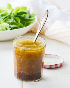 a jar filled with salad dressing next to a bowl of lettuce and a spoon