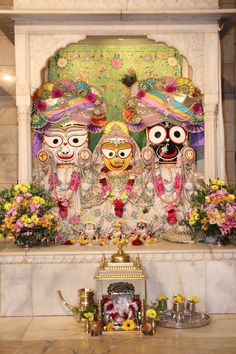 there are three masks on display with flowers in front of the wall and behind them is a shrine