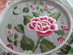 an embroidered rose on a gray background with green leaves and pink flowers in the center