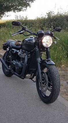 the motorcycle is parked on the side of the road next to some grass and bushes