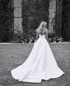 a woman in a wedding dress is standing on the grass near an ivy covered building