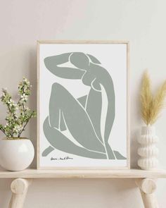 a white vase sitting on top of a wooden shelf next to a framed print with a nude woman