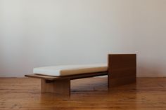 a wooden bench sitting on top of a hard wood floor next to a white wall