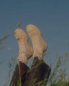 a person with their feet up in the air above some tall grass and weeds on a sunny day