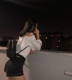 a woman standing on top of a balcony next to a wall with her hand in her pocket