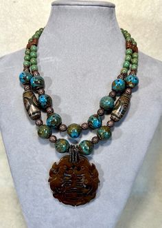 Double Strands Carved Old Jade Pendant Ceramic Turquoise Statement Necklace  Necklace is 17" long with 2 1/2" extension chain. The outer necklace with pendant is 19"long.  Carved Old Jade pendant is 2"x2" Hand made Ceramic turquoise beads are 14mm round (not by me) Czech glass green turquoise beads are 8mm round Tibet drum barrel Agate beads are 17mmx30mm Antique copper metal beads are 8mm round Acrylic metallic turquoise plated beads are 6mm round Antique brass bar ends and hook All metal findings are nickel and lead free Ancient Hand Carved Light Green Jade Large Pendant Necklace, Spiritual Turquoise Necklace With Patina, Spiritual Turquoise Patina Necklace, Traditional Blue Patina Necklace, Spiritual Turquoise Jade Necklace, Turquoise Jade Pendant Necklace, Bohemian Single Strand Jade Jewelry, Artisan Double Strand Turquoise Necklaces, Artisan Double Strand Turquoise Necklace