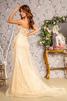 a woman in a wedding dress standing next to a table with flowers on the wall