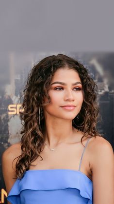 a woman with long curly hair and blue dress posing for the camera at an event