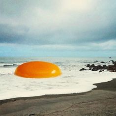 an orange object floating in the ocean on top of a sandy beach next to rocks