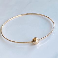 This cool single bangle was hand forged from 14kt gold fill wire and hammered with a dappled texture to catch the light.  It looks great stacked with other bangles you already  have but also fantastic on its own for a minimalist look. It features a 8mm 14kt gold fill ball that slides freely around the bangle. The diameter of the bangle is 2 1/2”. Custom sizing available upon request Solid Gold Bangle, Silver Bracelet Designs, Modern Gold Jewelry, The Bangles, Bracelets Design, Gold Fashion Necklace, Gold Gold, Diy Crafts Jewelry, Jewelry Lookbook