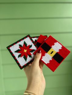 a hand holding two small pieces of cross - stitched christmas coasters in front of a green wall