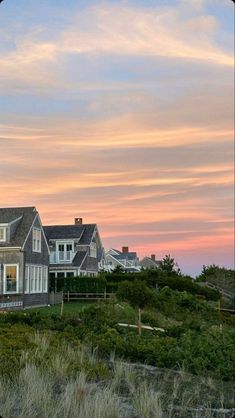 a large house sitting on top of a lush green hillside next to the ocean at sunset