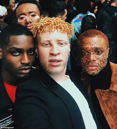 three men are posing for the camera in front of a group of people with brown hair