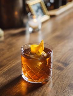 a glass filled with an orange peel on top of a wooden table