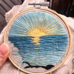 someone is holding up a hand embroidery project that looks like the sun rising over water