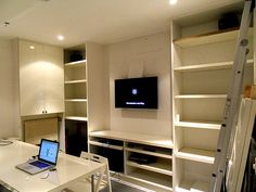 a laptop computer sitting on top of a white desk in front of a tv monitor