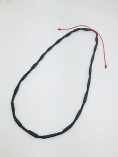 a long black beaded necklace with red string and beads hanging from it's end