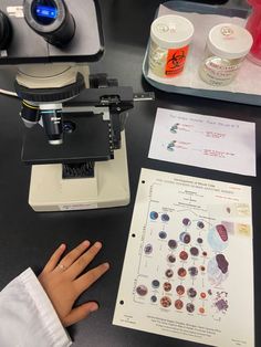 a person's hand is on the table next to a microscope and other items