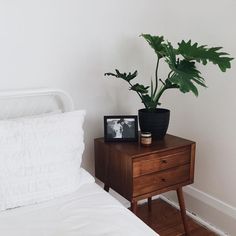 a bedroom with a bed, nightstand and potted plant on the end table in front of it