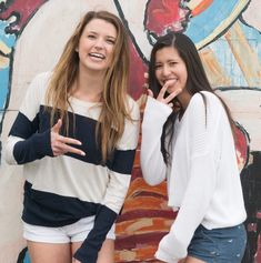 two young women standing next to each other in front of a wall painted with flowers