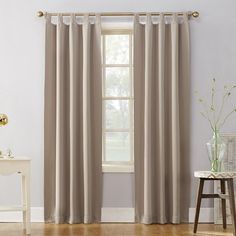 a living room with white walls and wooden flooring, two windows covered in beige curtains