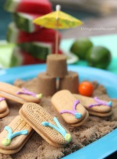 a blue plate topped with cookies covered in frosting next to an umbrella and sand