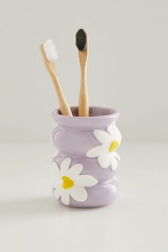 two toothbrushes in a purple cup with daisies