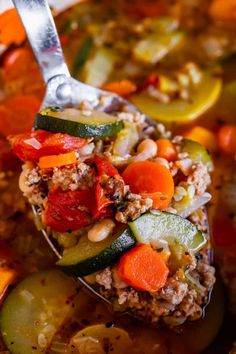 a spoon full of vegetable soup with meat and vegetables on the side, ready to be eaten