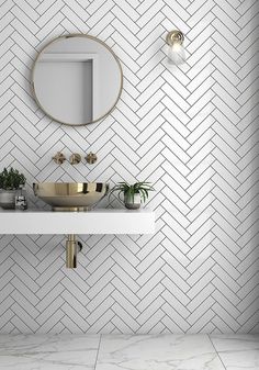 a white bathroom with gold accents and herringbone tiles on the wall, along with a round mirror