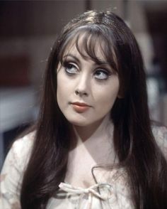 a woman with long dark hair and blue eyes wearing a white blouse is looking at the camera