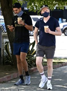 two men walking down the street wearing face masks and holding coffee cups in their hands