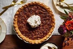 a pecan pie with whipped cream on top sits on a table next to plates and forks