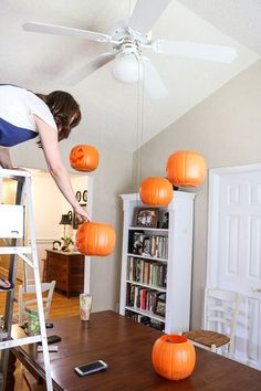 a woman is decorating pumpkins on the ceiling in her living room with ladder