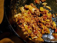 a skillet filled with meat and vegetables on top of a wooden table