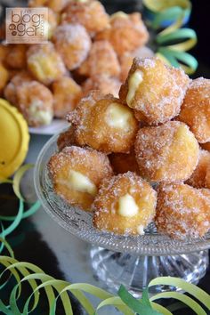 some sugared donuts are in a glass bowl on a table next to other desserts