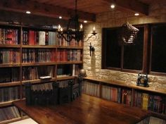 a room filled with lots of books and a wooden table in front of a window