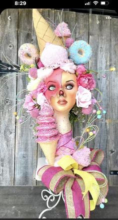 a doll with pink hair and ice cream cones on it's head, sitting in front of a wooden wall